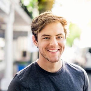 Close-up portrait of young man. Smiling handsome male is wearing casuals. He is in city on sunny day.